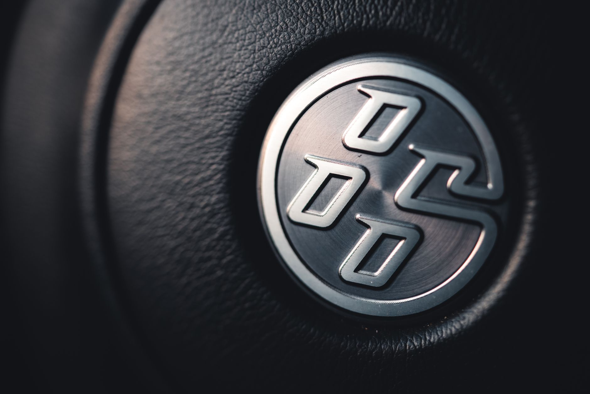Detailed close-up of a sleek silver car emblem on a textured black leather background.