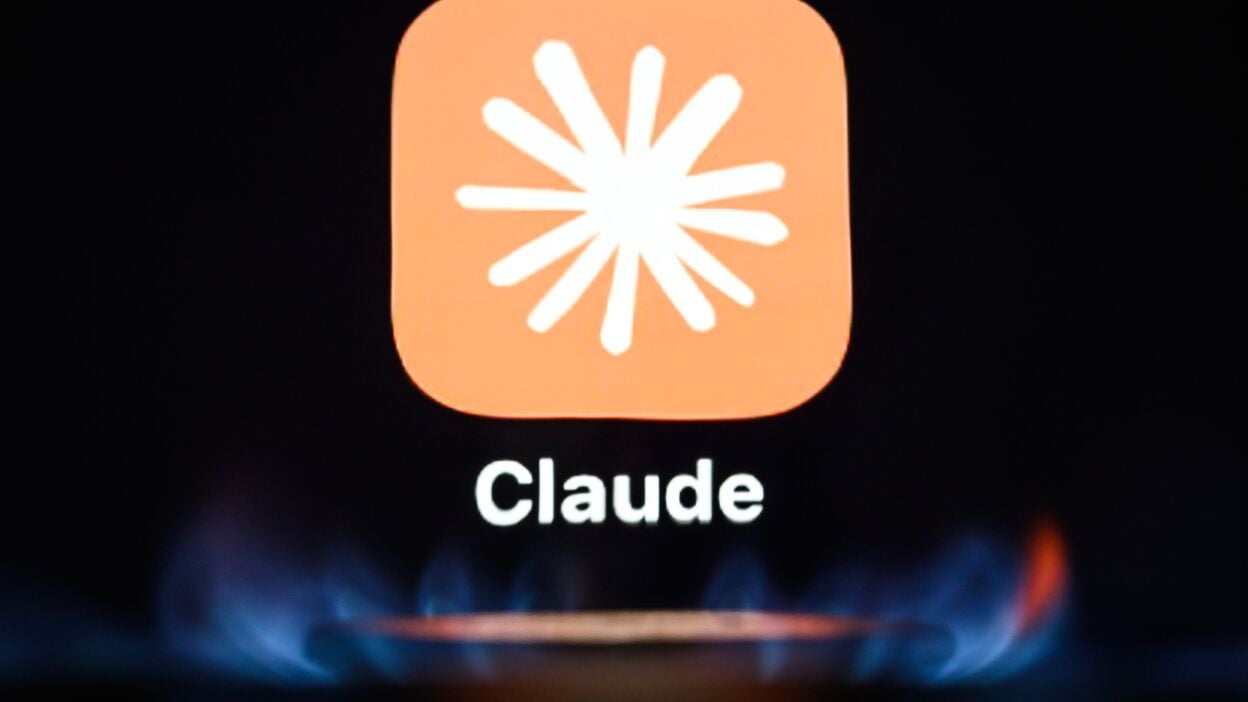 the icon for the AI app "Claude" by Anthropic is seen through a flame as it is displayed on a digital screen